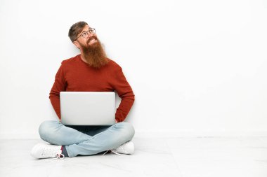 Dizüstü bilgisayarı olan genç, beyaz arka planda izole edilmiş beyaz bir adam yukarı bakarken bir fikir düşünüyor.