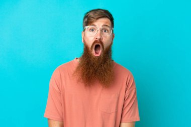 Mavi arka planda gözlüklü ve şaşkın bakışlı genç, beyaz bir adam.