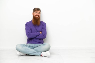 Beyaz arka planda soyutlanmış, kolları bağlı, yerde oturan beyaz tenli genç bir adam.