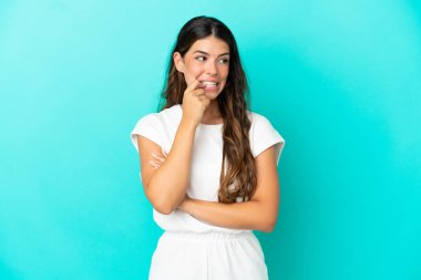 Mavi arka planda izole edilmiş genç beyaz kadın gergin ve korkmuş.