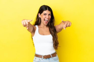 Sarı arka planda izole edilmiş genç beyaz kadın şaşırmış ve ön tarafı işaret ediyor.