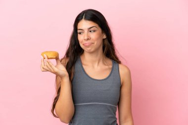 Pembe arka planda izole edilmiş genç beyaz kadın elinde donutlarla