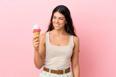 Kornet dondurması olan beyaz bir kadın pembe arka planda izole edilmiş, yana bakıyor ve gülümsüyor.
