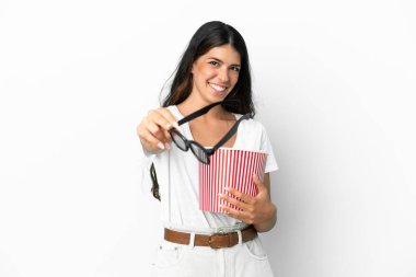 Beyaz arka planda 3 boyutlu gözlüklü ve elinde koca bir kova patlamış mısır tutan beyaz tenli bir kadın.