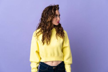 Mor arka planda izole edilmiş genç beyaz kadın yan tarafa bakıyor.