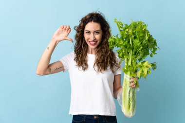 Mavi arka planda kendini beğenmiş ve gururlu bir kereviz tutan genç kadın.