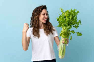 Mavi arka planda izole edilmiş bir kereviz taşıyan genç kadın zaferi kutluyor.