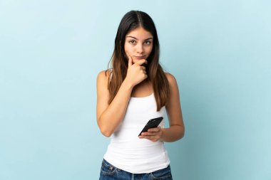 Mavi arka planda izole edilmiş cep telefonu kullanan beyaz bir kadın.