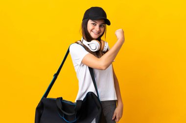 Sarı arka planda izole edilmiş spor çantalı genç bayan güçlü bir jest yapıyor.