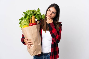 Beyaz arka planda izole edilmiş sebzeleri olan genç bir beyaz. Şüpheleri var.