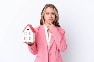 Rus emlakçı elinde oyuncak ev tutuyor. Beyaz arka planda izole edilmiş. Şüpheleri var.