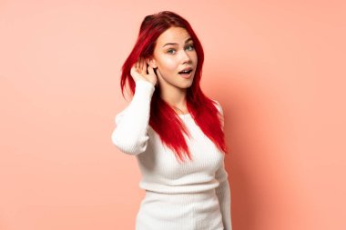 Genç kızıl saçlı kız pembe arka planda izole edilmiş. Kulağına elini sürerek bir şeyler dinliyor.