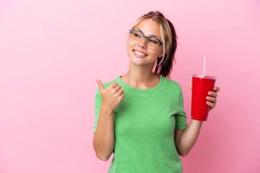 Pembe arka planda izole edilmiş bir içecek taşıyan genç Rus kadın bir ürünü sunmak için kenarı işaret ediyor.