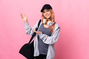 Spor çantalı genç bayan izole edilmiş arka planda ellerini yana uzatarak davet ediyor.