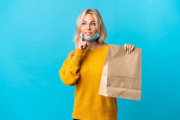 Junge Russin Hält Eine Einkaufstasche Mit Lebensmitteln Auf Blauem Hintergrund — Stockfoto