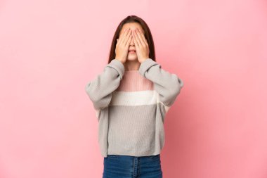 Pembe arka planda izole edilmiş küçük bir kız gözlerini elleriyle kapatıyor.