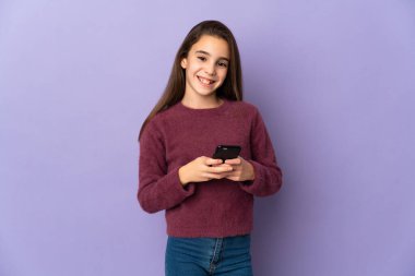 Mor arka planda izole edilmiş küçük bir kız cep telefonuyla mesaj gönderiyor.