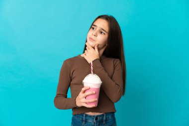 Mavi arka planda izole edilmiş çilekli milkshake 'i olan küçük bir kız şüpheleri var.
