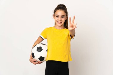 Beyaz arka planda izole edilmiş küçük futbolcu kız gülümsüyor ve zafer işareti gösteriyor.