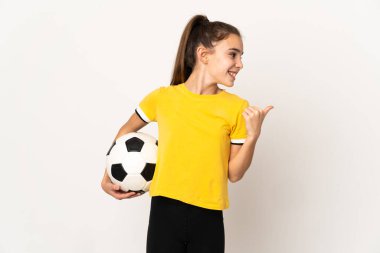 Beyaz arka planda izole edilmiş küçük futbolcu kız bir ürünü sunmak için kenarı işaret ediyor.