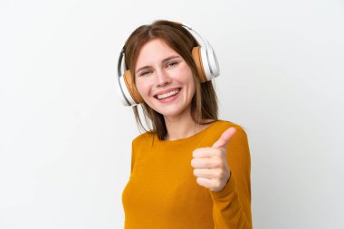 Beyaz arka planda izole edilmiş genç bir İngiliz kadın müzik dinliyor ve başparmağını kaldırıyor.