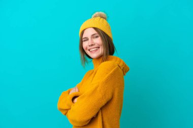 Kışlık ceket giyen genç İngiliz kadın mavi arka planda izole edilmiş, kolları bağlı ve ileriye bakıyor.