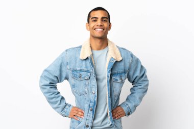 Beyaz arka plan üzerinde kolları kalçasında poz veren ve gülümseyen Afrikalı Amerikalı bir adam.