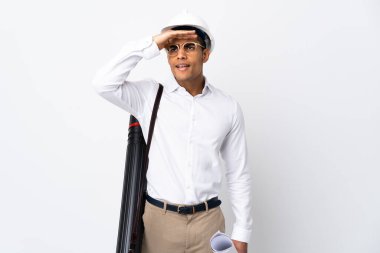 African American architect man with helmet and holding blueprints over isolated white background _ looking far away with hand to look something