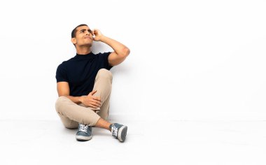 Afro-Amerikalı bir adam yerde oturuyor ve kafası karışık.