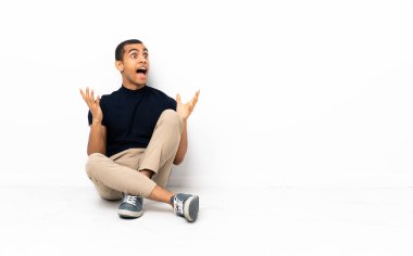 Afro-Amerikalı bir adam yerde oturuyor ve yüzünde sürpriz bir ifade var.