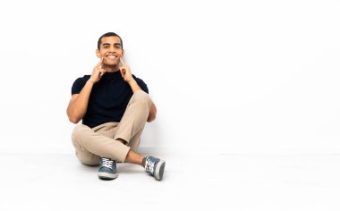 African American man sitting on the floor smiling with a happy and pleasant expression