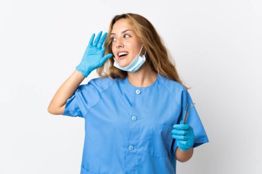 Woman dentist holding tools isolated on white background listening to something by putting hand on the ear