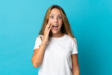 Genç sarışın kadın mavi arka planda izole edilmiş, şaşırmış ve şok olmuş bir yüz ifadesi var.