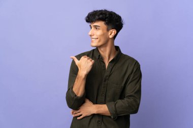 Arka planda izole edilmiş genç Arjantinli bir adam bir ürün sunmak için kenarı işaret ediyor