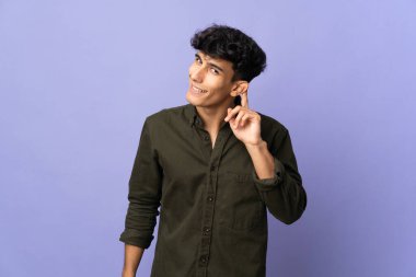 Arjantinli genç adam arka planda izole edilmiş bir şekilde bir şeyler dinlerken elini kulağına koydu.