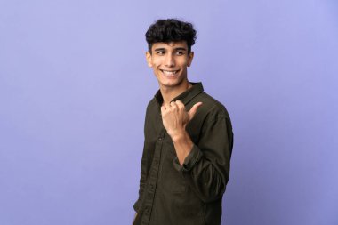 Arka planda izole edilmiş genç Arjantinli bir adam bir ürün sunmak için kenarı işaret ediyor