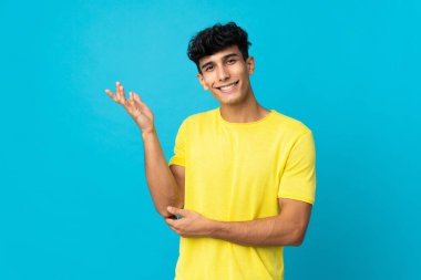 Arjantinli genç adam arka planda izole edilmiş. Davet etmek için ellerini yana uzatıyor.