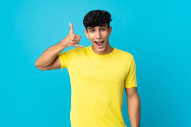 Arjantinli genç bir adam arka planda izole edilmiş, telefon jesti yapıyor. Bana geri dönüş işareti ver.