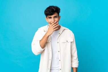 Arjantinli genç adam arka planda izole edilmiş mutlu ve gülümseyen ağızlarını eliyle kapatıyor.