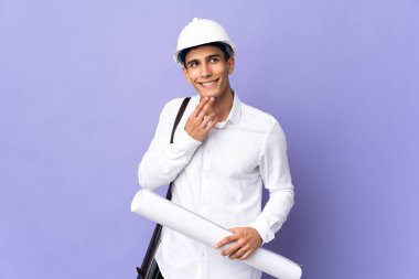 Young architect man isolated on background looking up while smiling