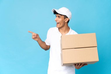 Delivery Argentinian man isolated on blue background pointing finger to the side and presenting a product