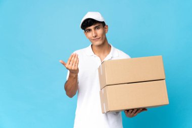 Delivery Argentinian man isolated on blue background inviting to come with hand. Happy that you came