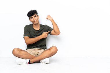 Young Argentinian man sitting on the floor doing strong gesture