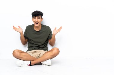 Young Argentinian man sitting on the floor with shocked facial expression