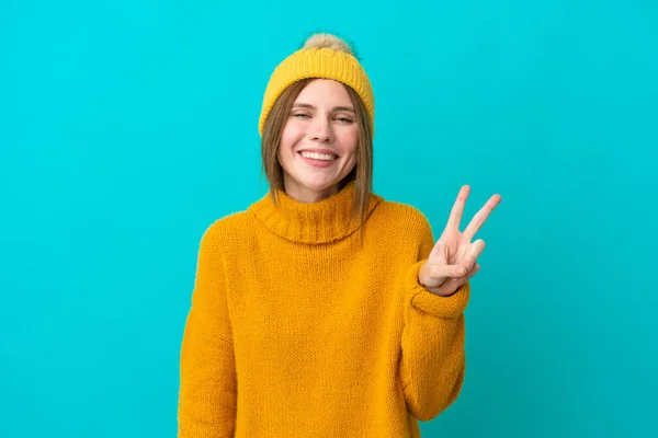 Junge Engländerin Winterjacke Auf Blauem Hintergrund Lächelt Und Zeigt Siegeszeichen — Stockfoto