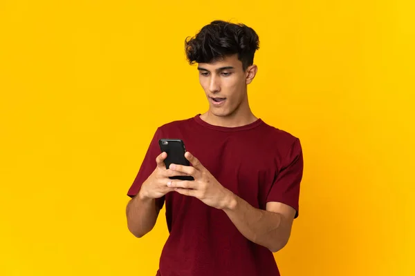 Young Argentinian Man Isolated Yellow Background Looking Camera While Using — Zdjęcie stockowe