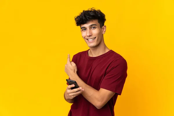 Young Argentinian Man Isolated Yellow Background Using Mobile Phone Pointing — Stockfoto