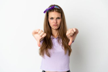 İzole edilmiş arka planda genç beyaz bir kadın baş parmağını iki eliyle aşağı gösteriyor.