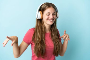 Genç beyaz kadın mavi arka planda izole edilmiş müzik ve dans dinliyor.