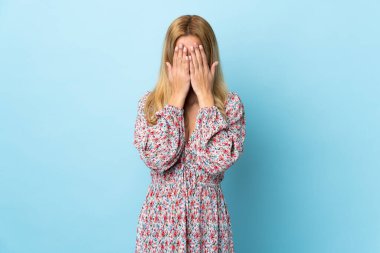 Genç Uruguaylı sarışın kadın izole edilmiş mavi arka planda gözlerini elleriyle kapatıyor.